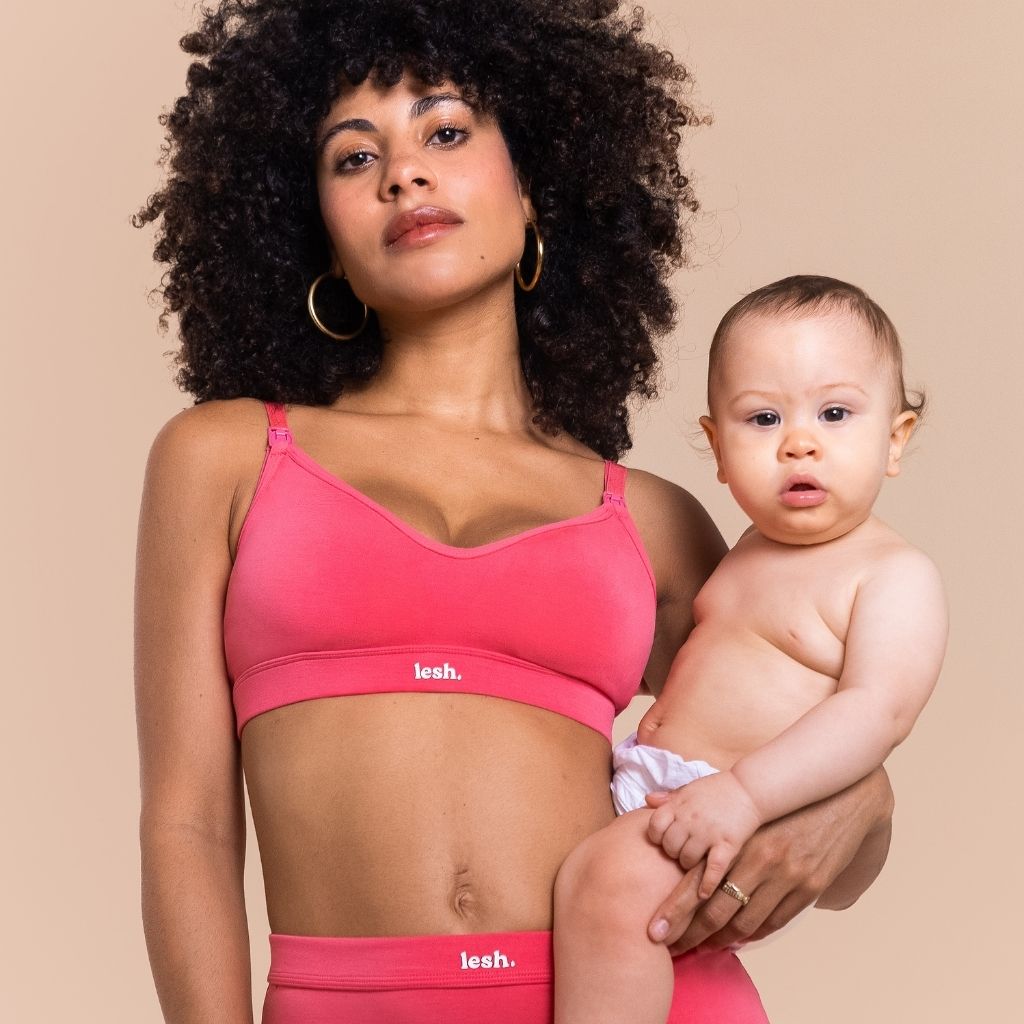 Woman holding a baby wearing a neon pink nursing bra