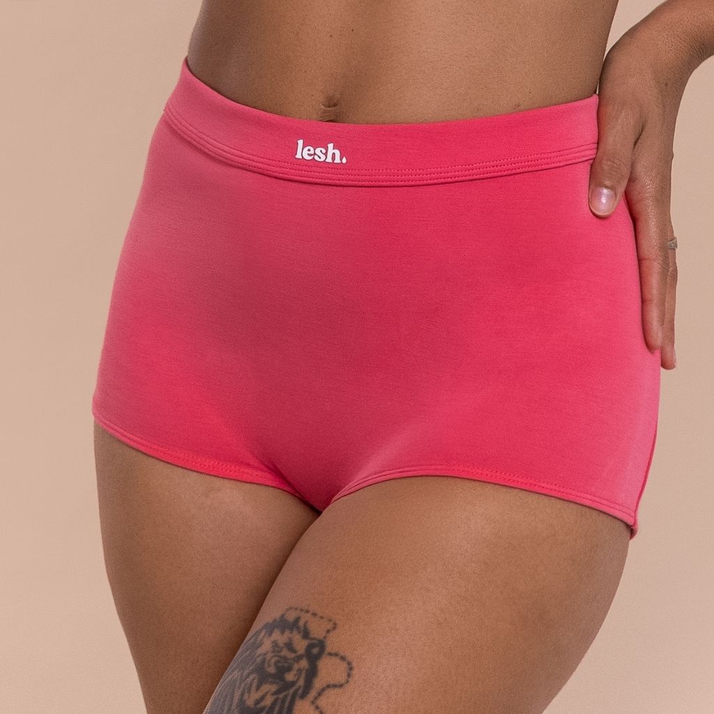 Person wearing pink underwear with 'lesh' brand logo on a beige background