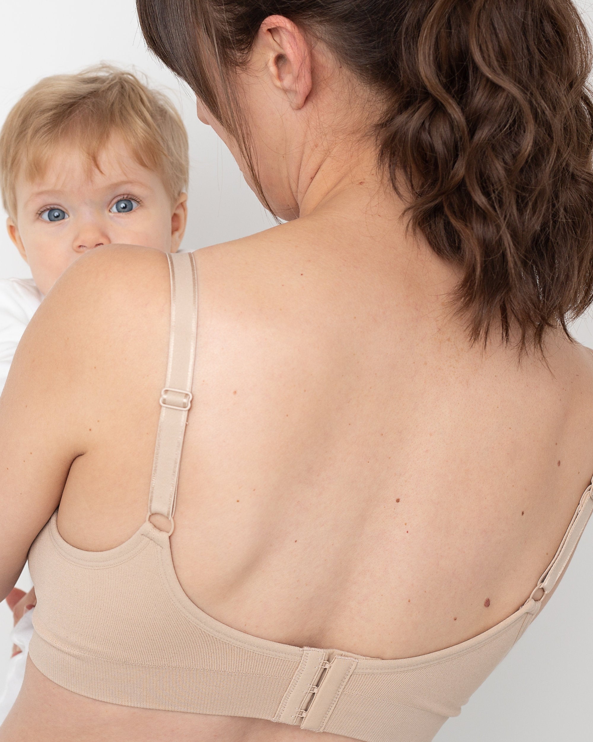 Woman wearing a white nursing bra holding a baby against a white background