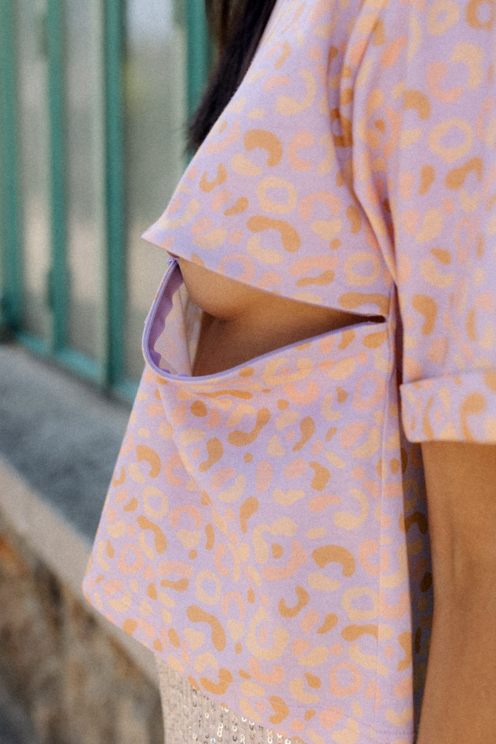 Person wearing a light pink leopard print T-shirt with nursing zip opened against a textured wall.