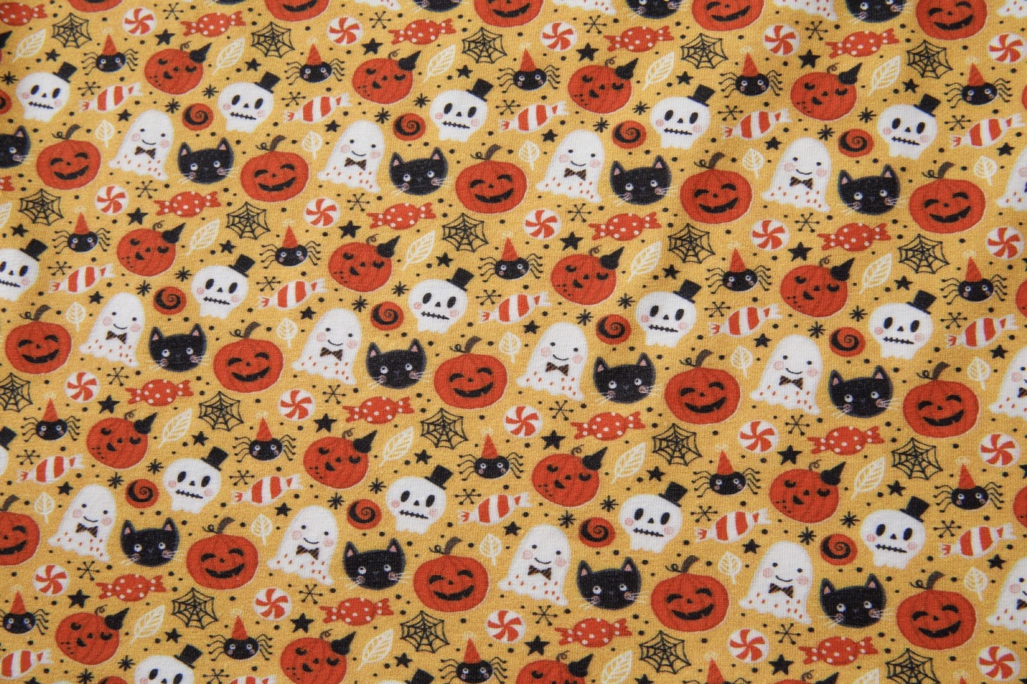 Halloween-themed fabric with pumpkins, ghosts, cats, and candy on a yellow background.