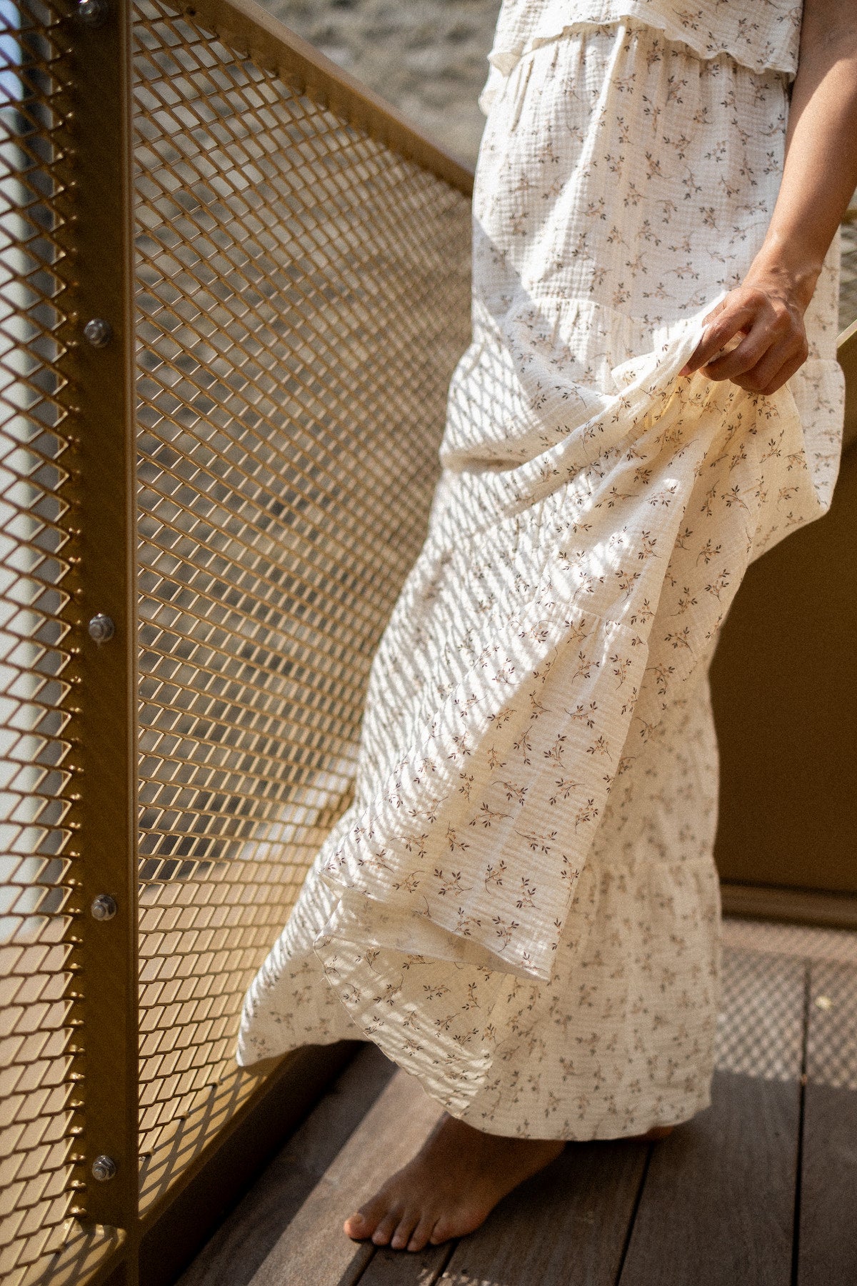 Person wearing a long, light-colored dress with a subtle pattern, standing on a wooden deck.