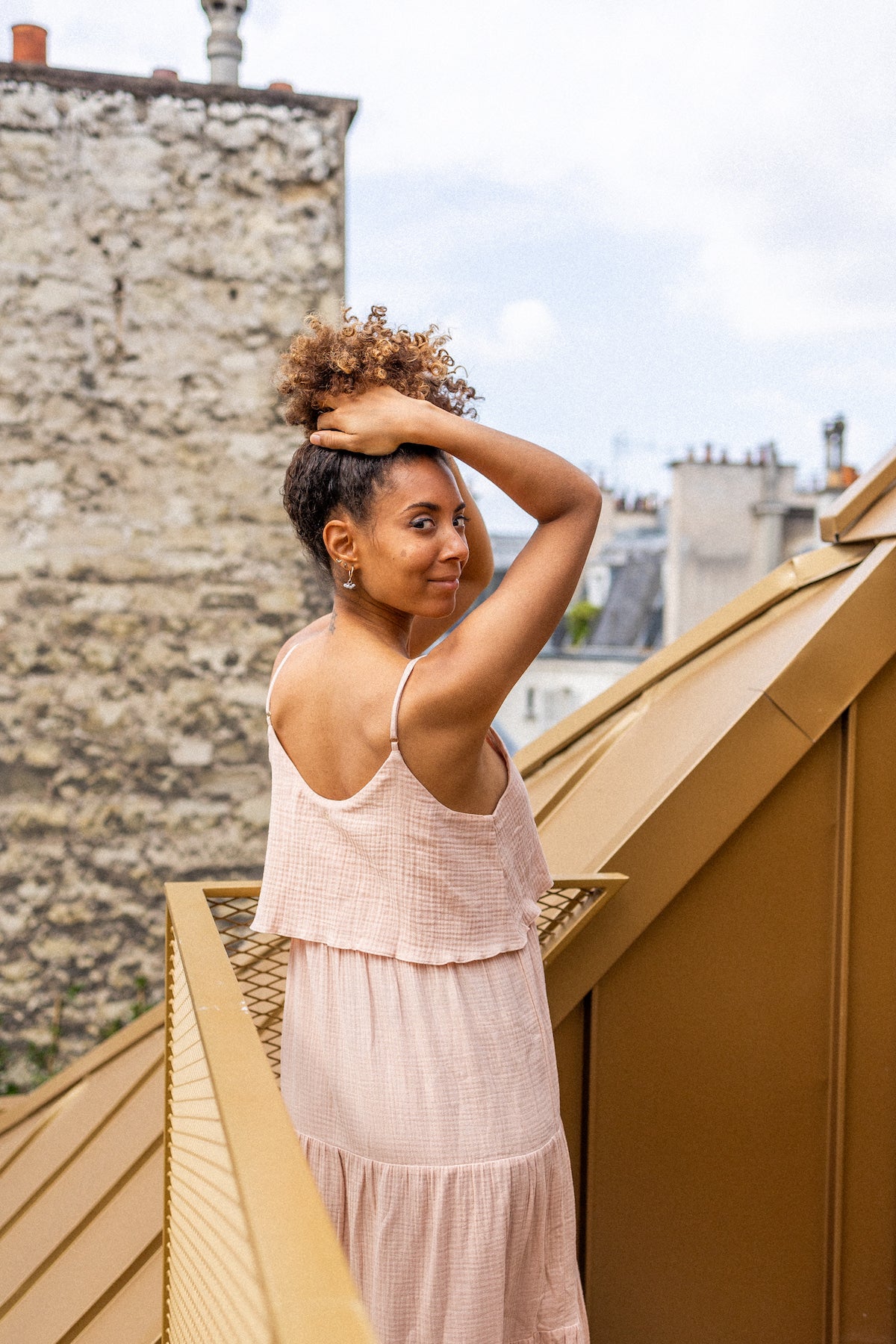 Woman in a long nude dress standing on a rooftop with a cityscape background