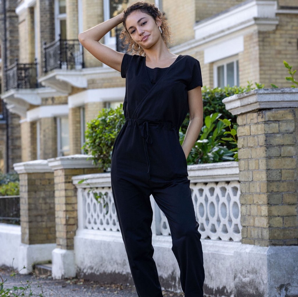Woman wearing a black jumpsuit standing in front of a brick building.