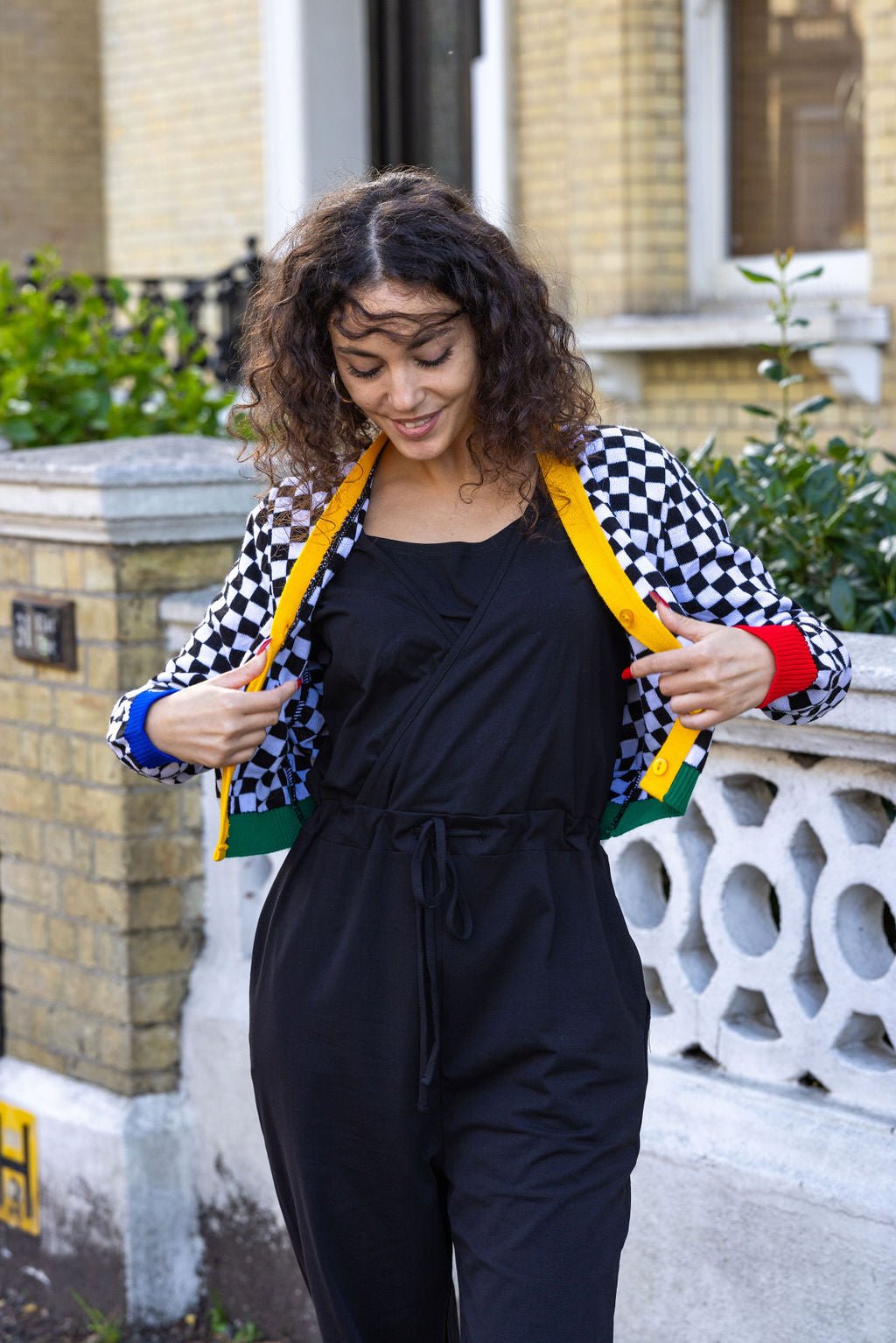Woman wearing a black jumpsuit with a colorful checkered jacket in an urban setting.