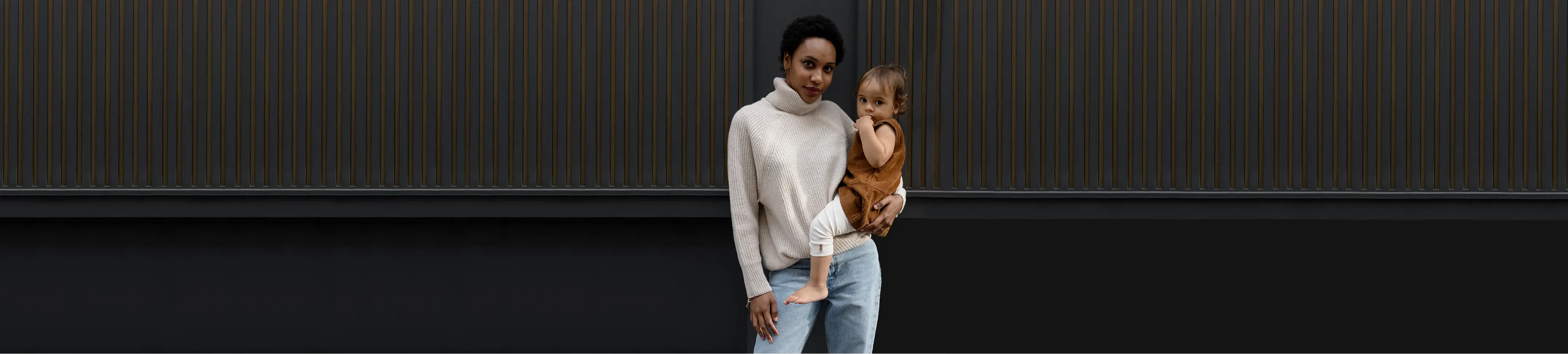 women with a white wool jumper carrying a baby  on a dark background