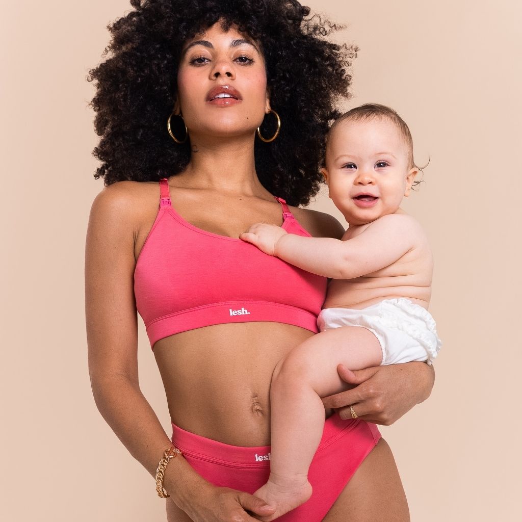 Woman in pink lingerie holding a baby against a beige background