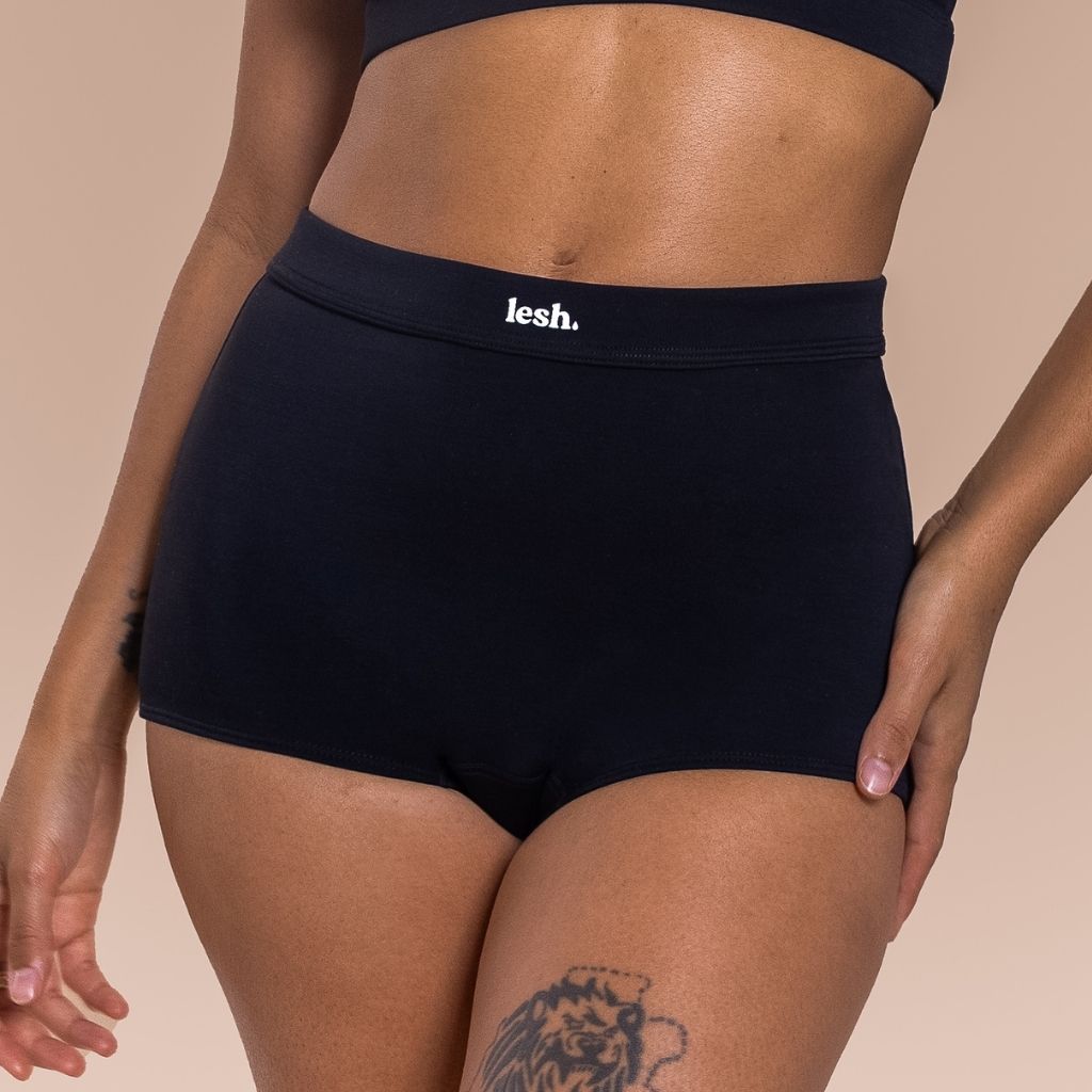 Woman wearing black underwear with 'lesh' branding on a beige background