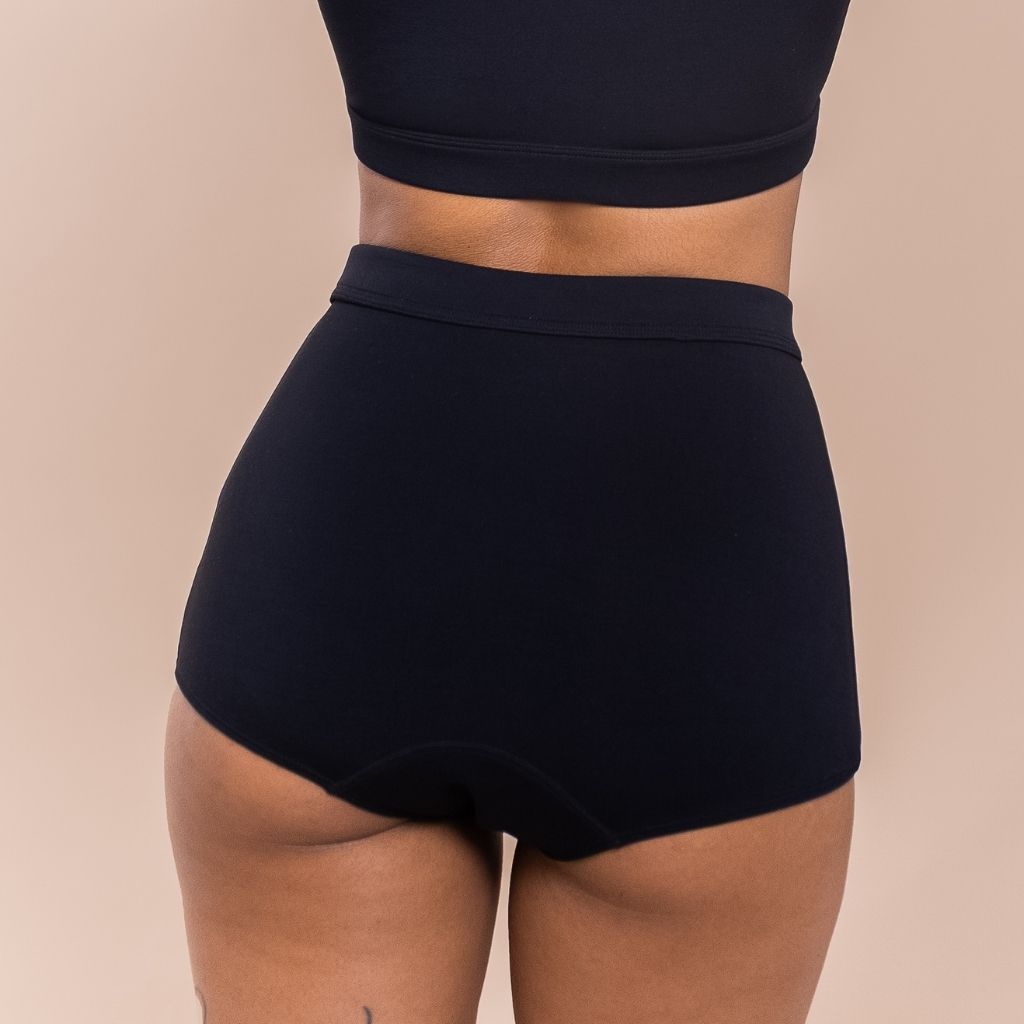 Black high-waisted shorts worn by a woman  on a beige background