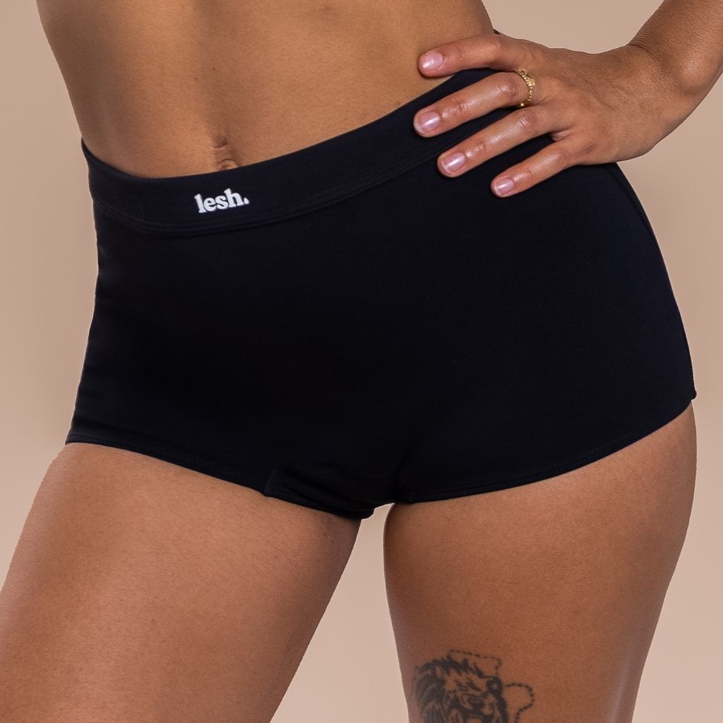 Woman wearing black underwear with 'lesh' brand logo on a beige background