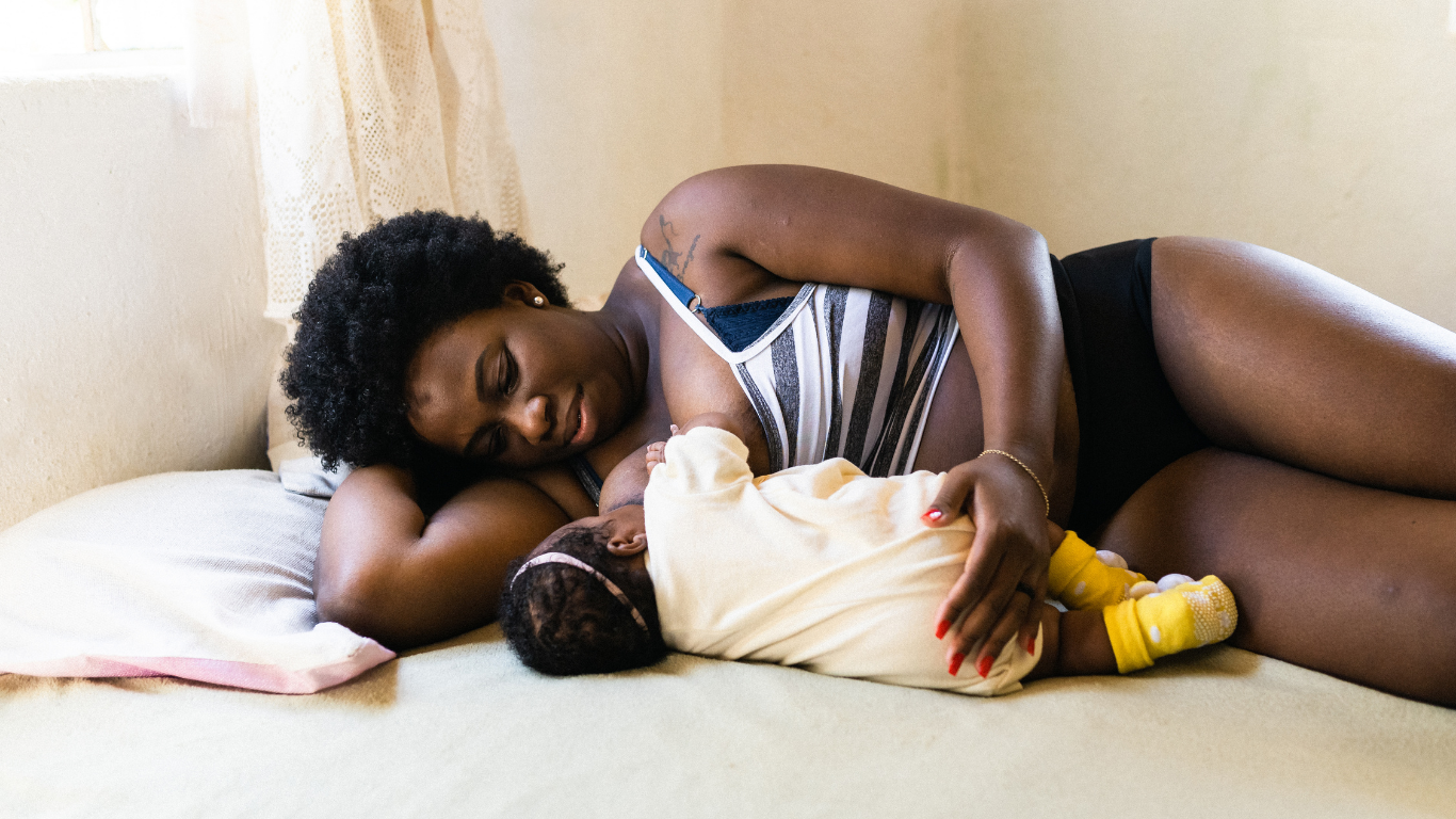 woman lying on her side in bed facing her baby and breastfeeding