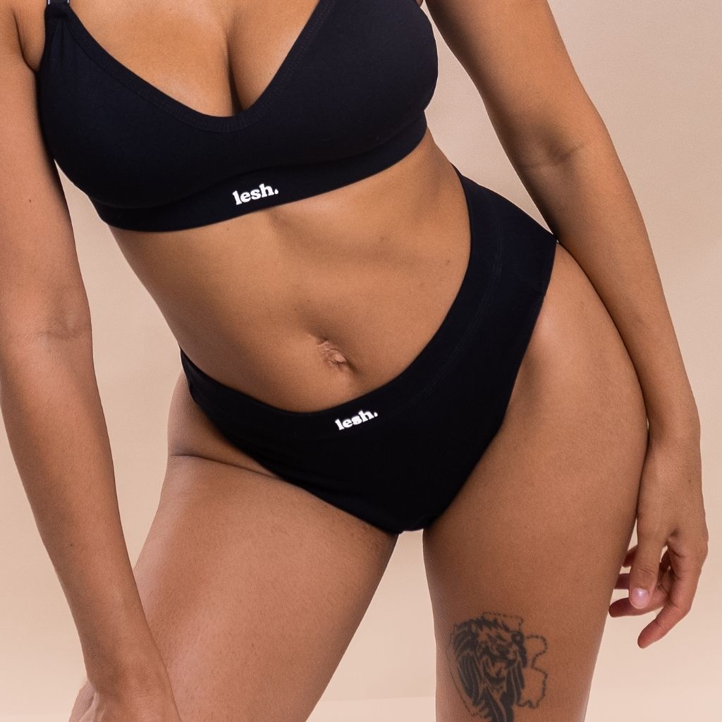 Person wearing a black bikini with 'lesh' branding on a beige background