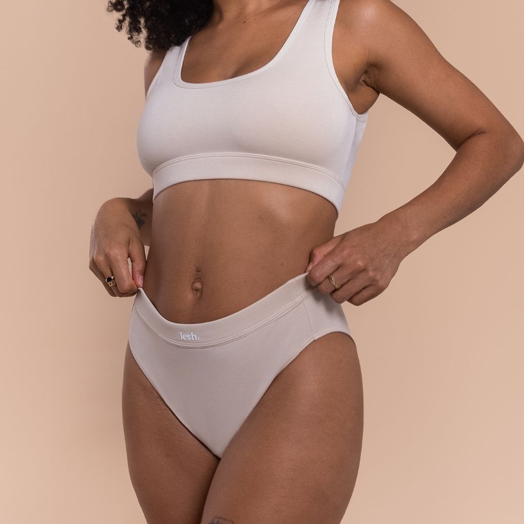 Person wearing a sports bra and beige high-waisted underwear on a beige background