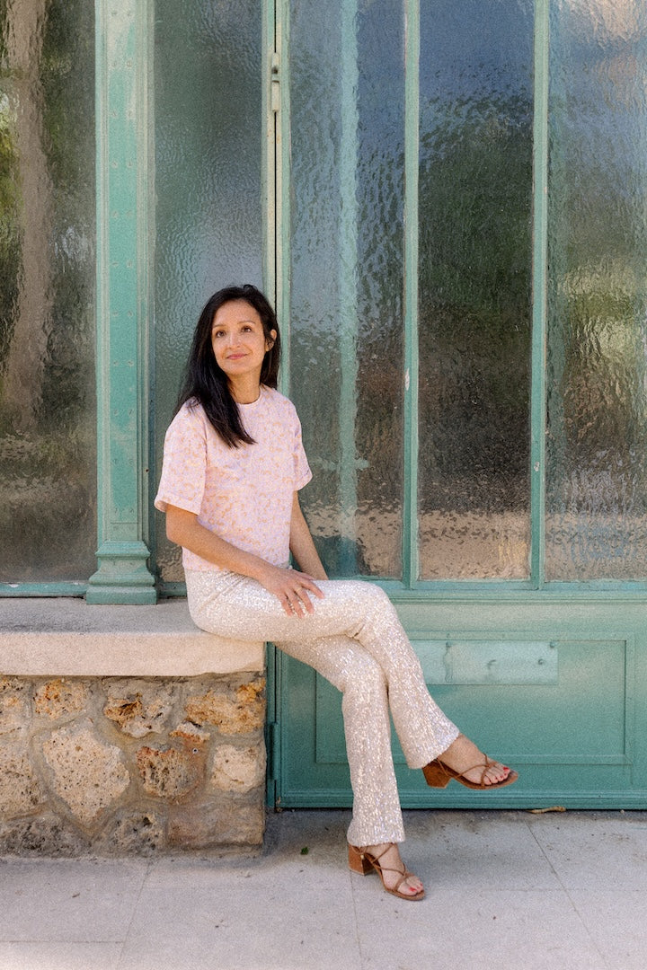 Woman sitting outdoors wearing a pink leopard print T-shirt against a textured wall.