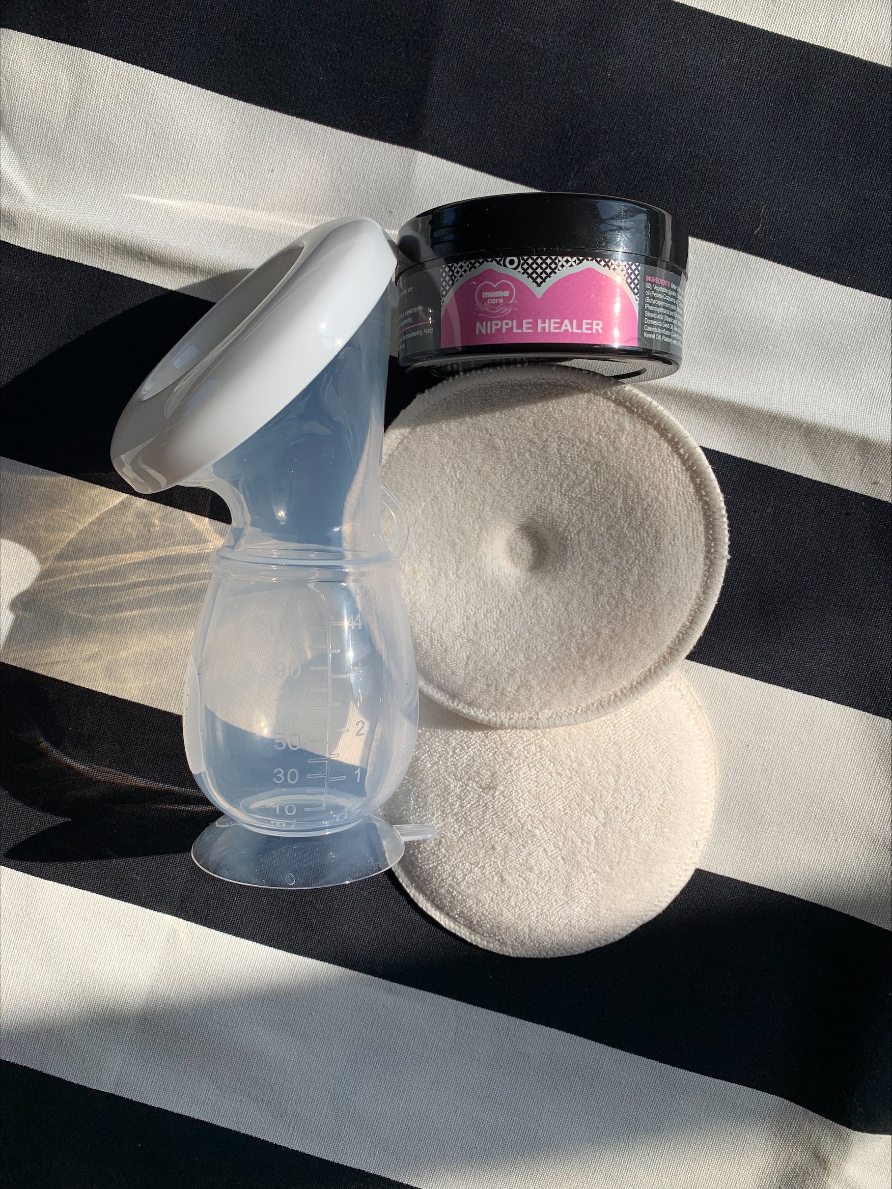 Breast pump, pads, and a container on a black and white striped background