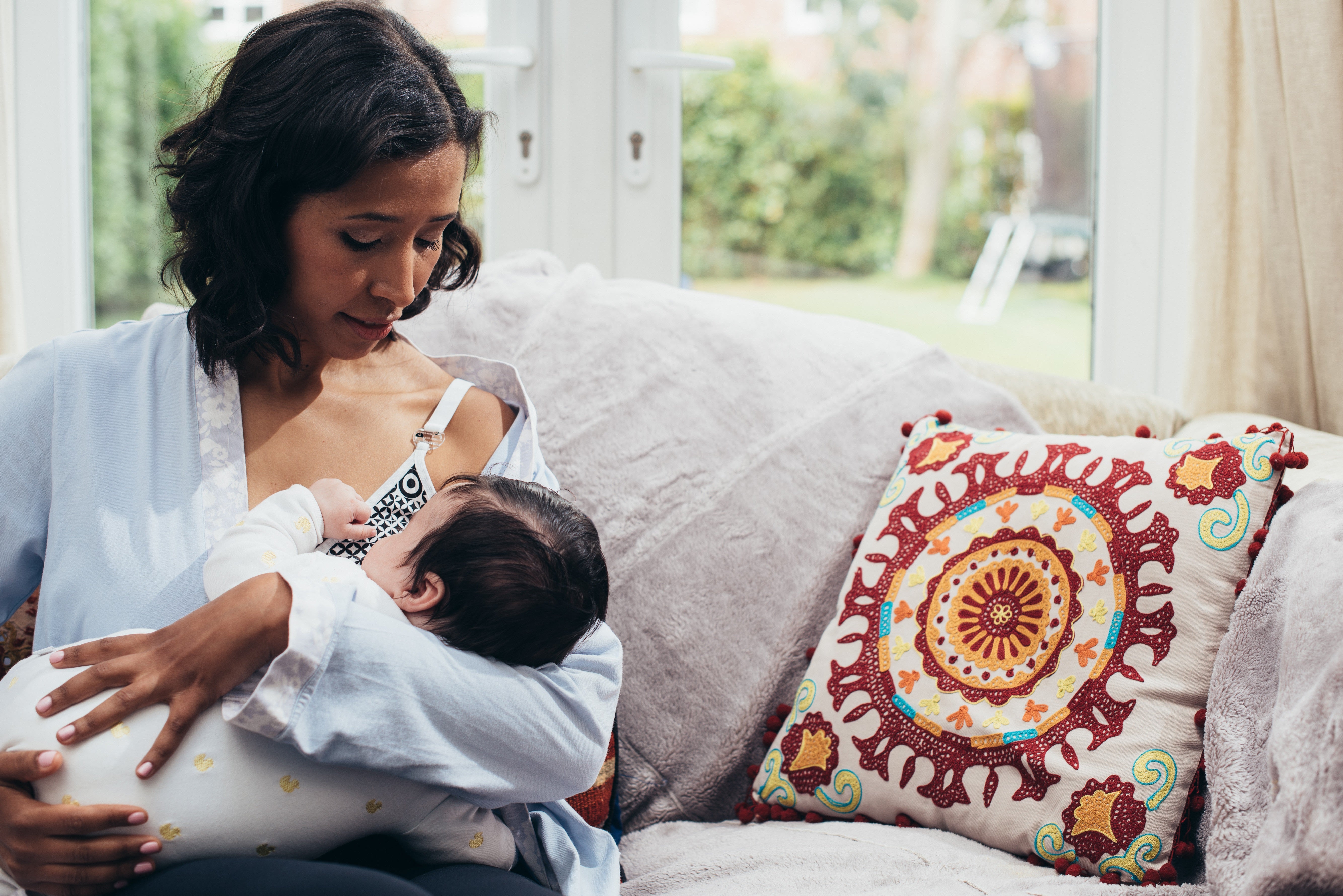 Woman breastfeeding a baby on a couch with a colorful pillow in the background