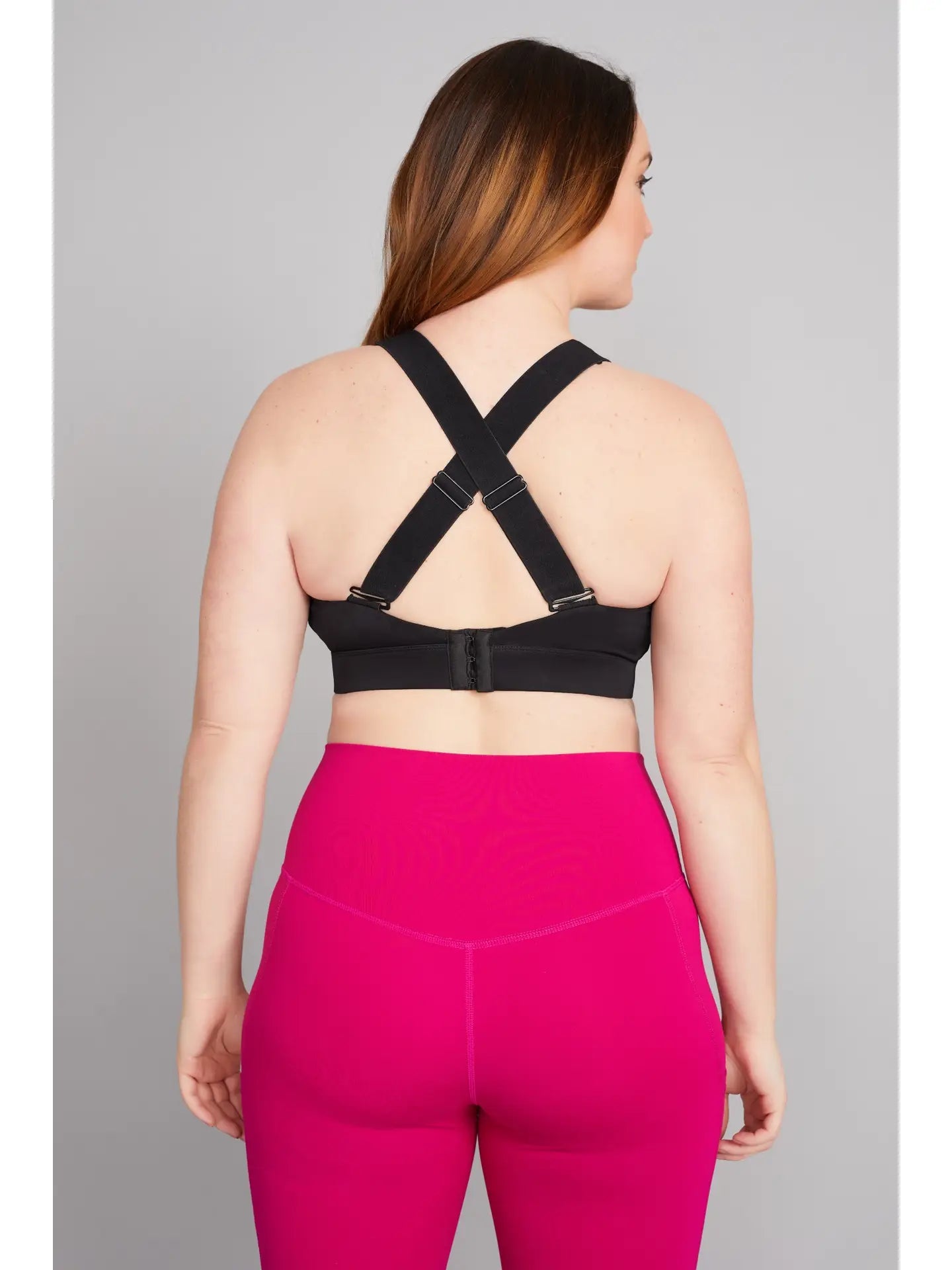Woman wearing a black sports bra and pink leggings on a gray background