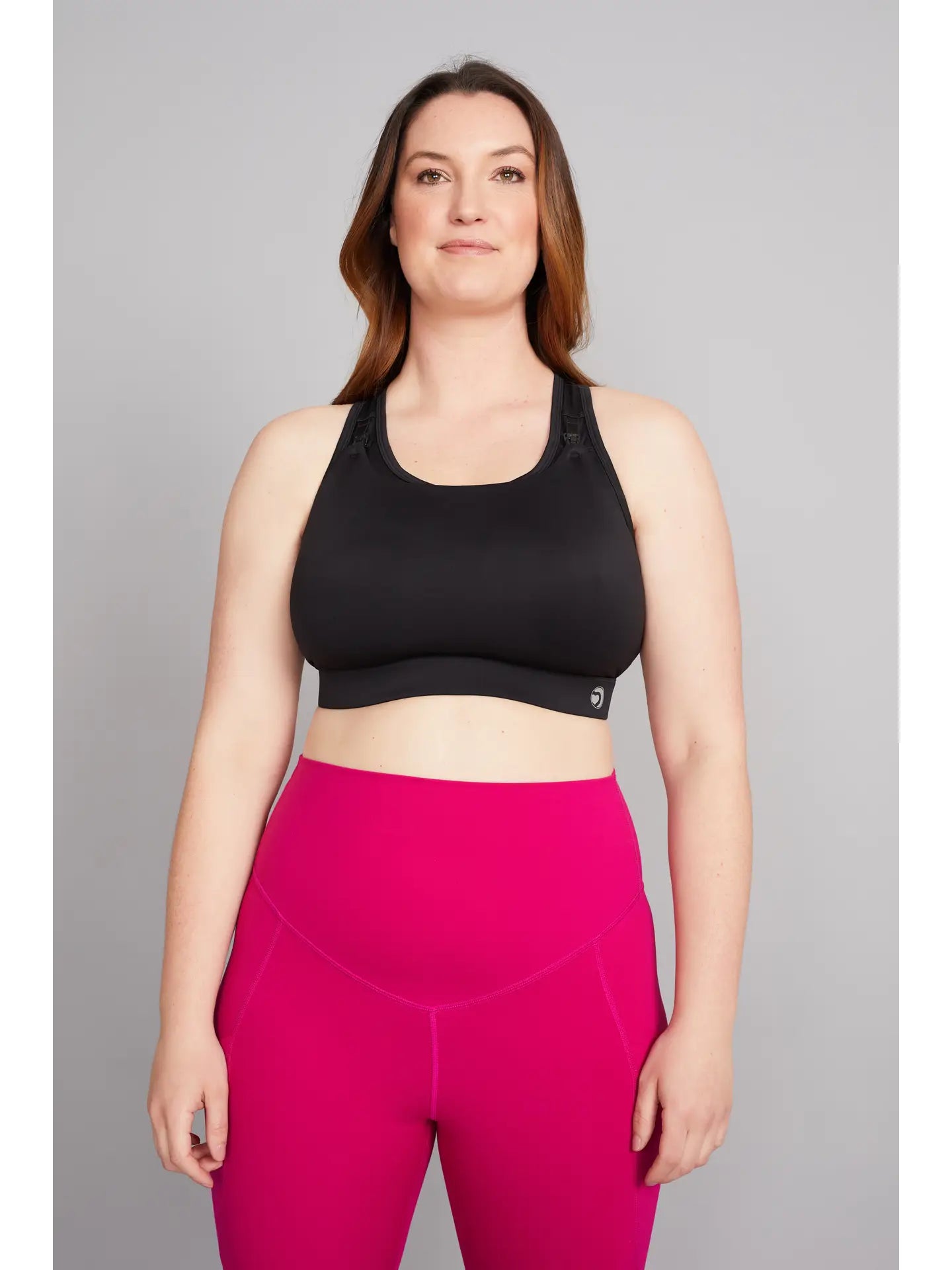 Woman wearing a black sports bra and pink leggings on a gray background