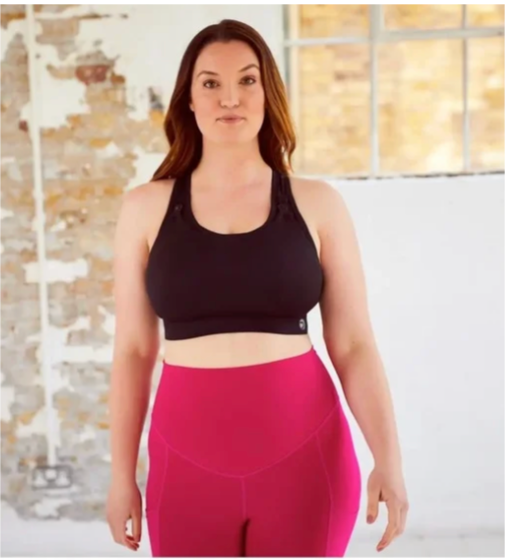 Woman wearing a black sports bra and pink leggings indoors.