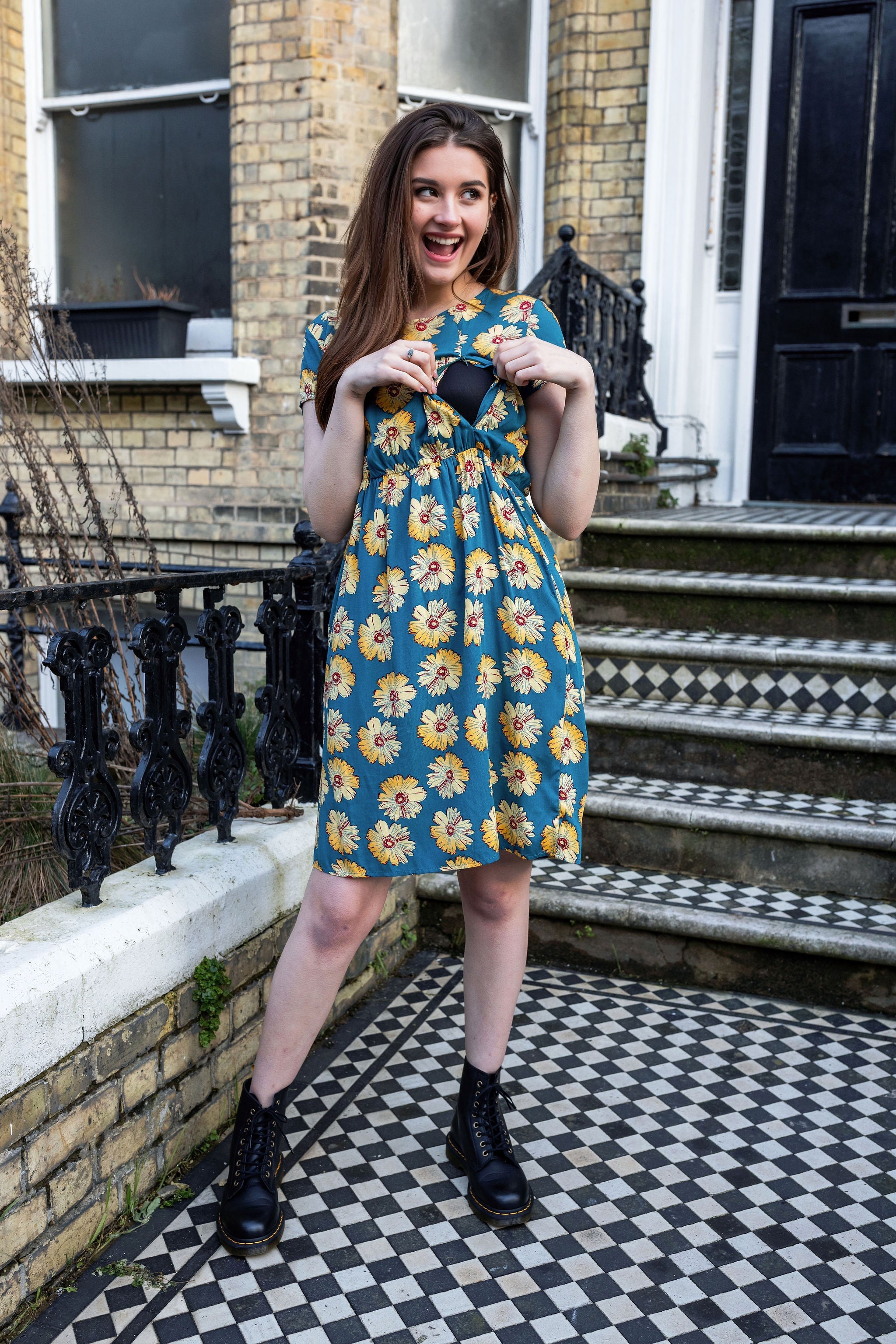 Woman in a floral dress standing on a checkered pavement outside a building.