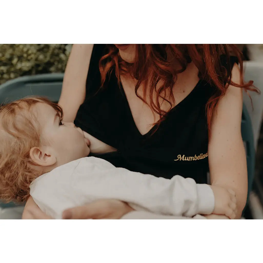 Woman with black top nursing a child outdoors with plants and a bench in the background