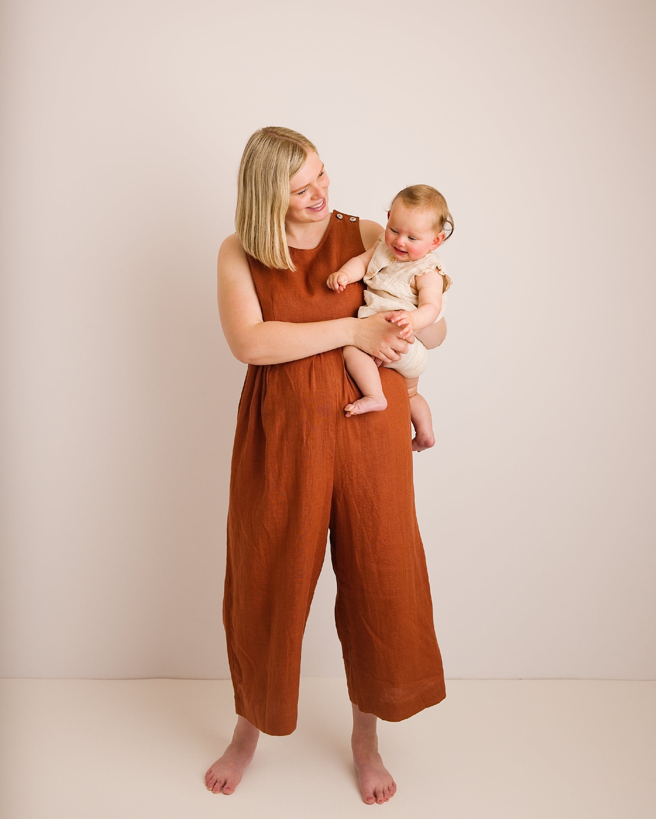 Woman in a brown jumpsuit holding a baby against a plain background