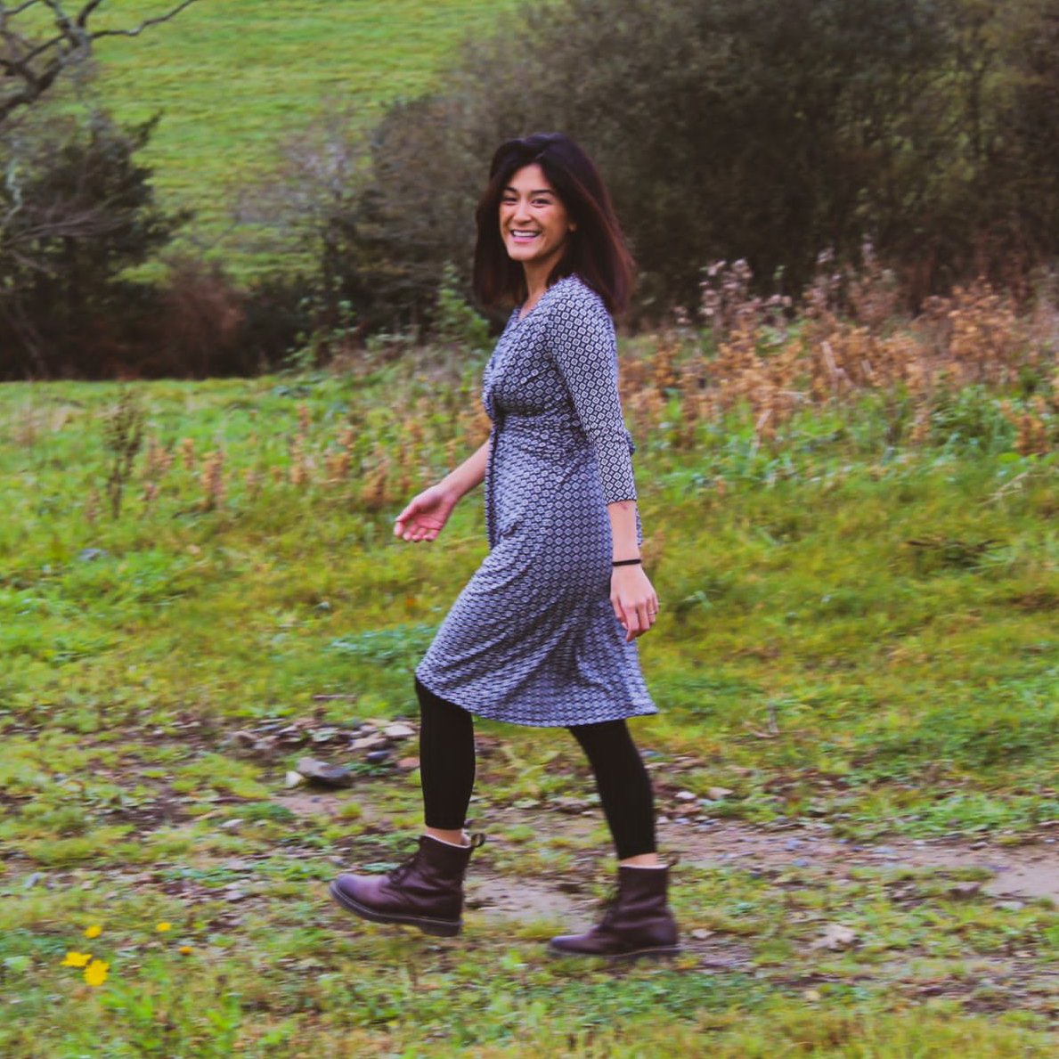 Woman in a patterned dress standing in a grassy field with trees in the background