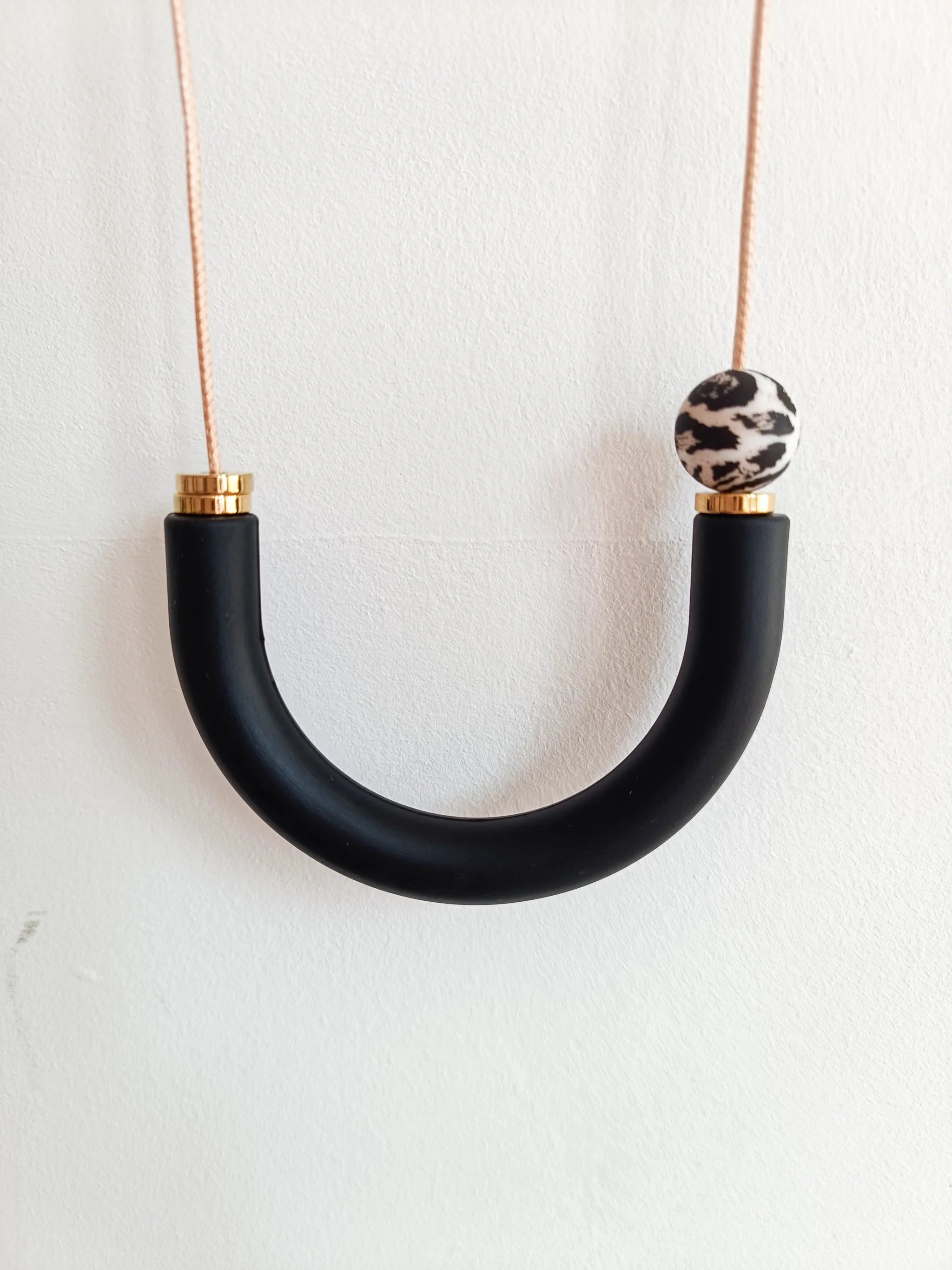 Black U-shaped necklace with a leopard print bead on a white background