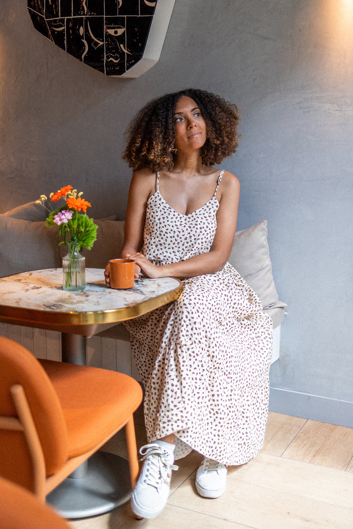 Woman sitting at a table with a cup and flowers, wearing a subtle leopard print long dress 