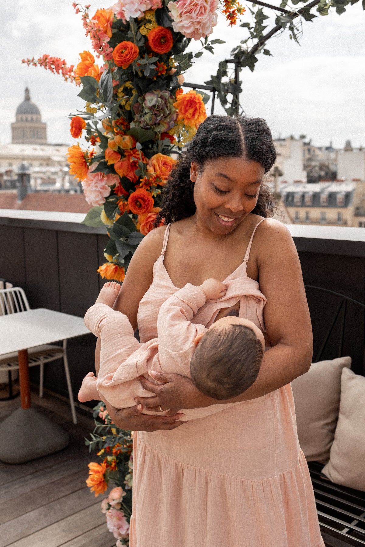 Woman breastfeeding a baby on a rooftop with floral decorations and cityscape in the background