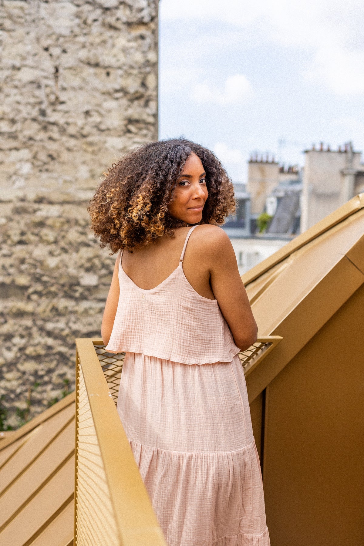 Woman in a long nude dress standing on a rooftop with a cityscape in the background