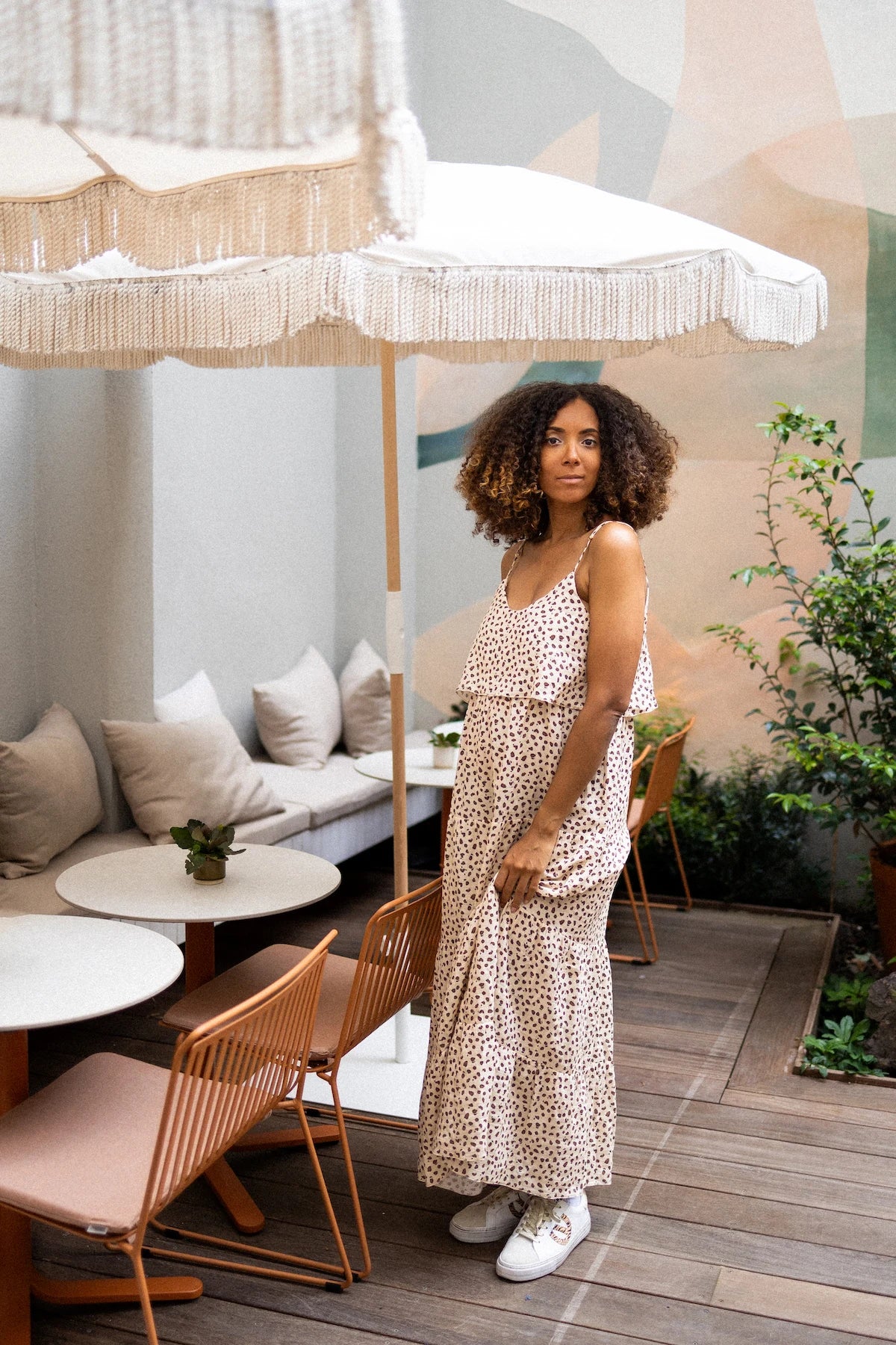 Woman in a subtle leopard print long dress standing under a large decorative umbrella in an outdoor cafe setting.