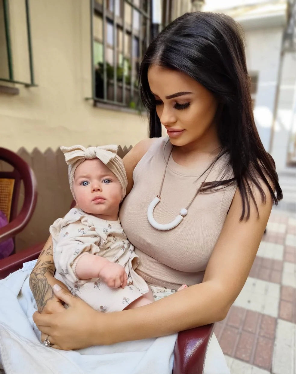 Woman wearing a U-shaped breastfeeding necklace holding a baby in an outdoor setting
