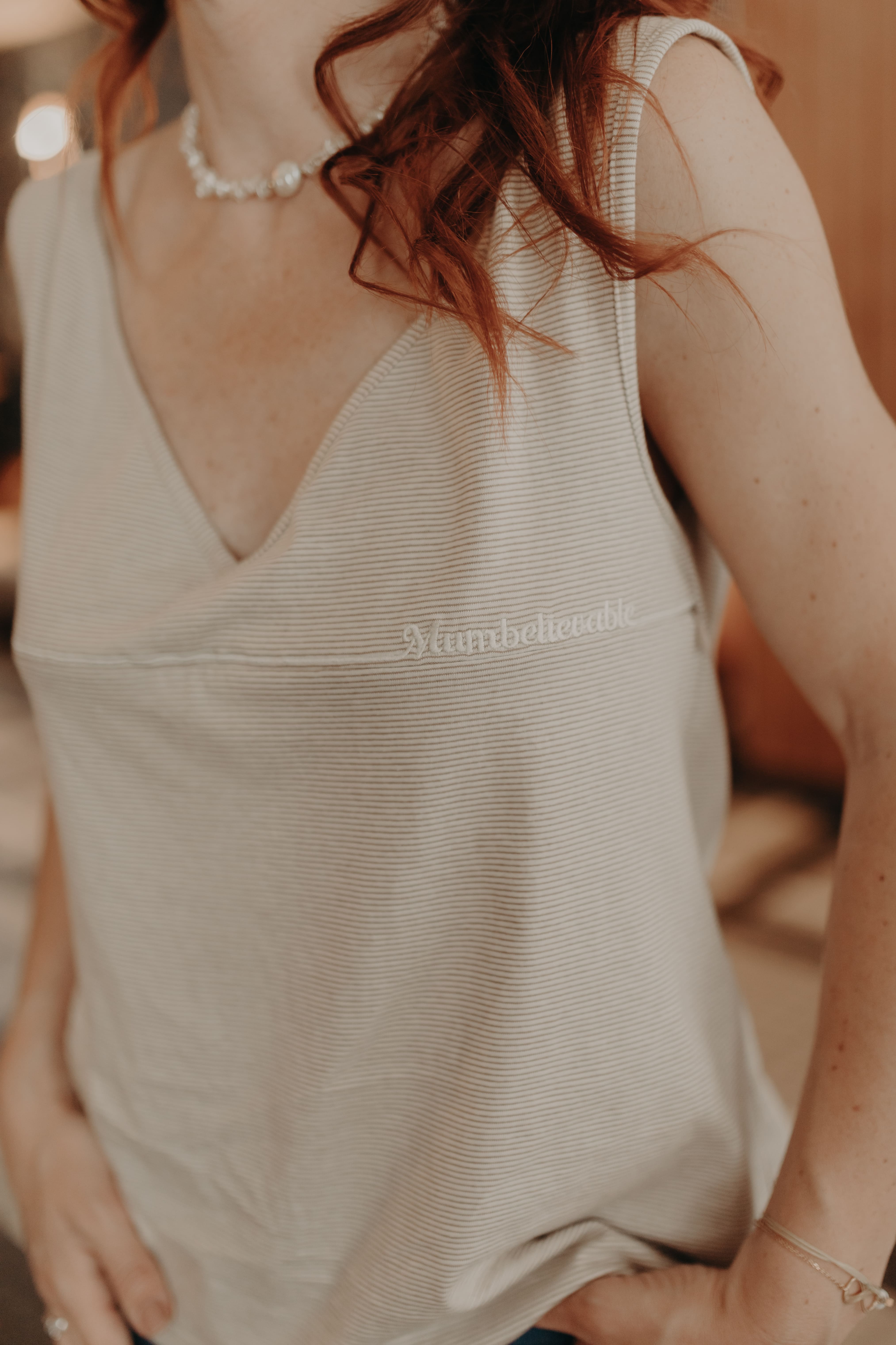 Woman wearing a beige sleeveless top with 'Mumbelievable' subtle golden text.