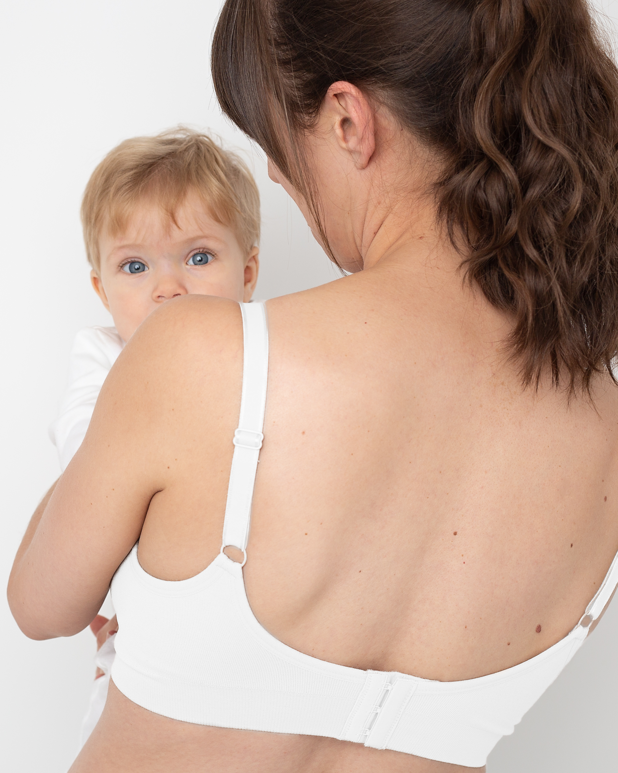 Woman wearing a white nursing bra holding a baby against a white background
